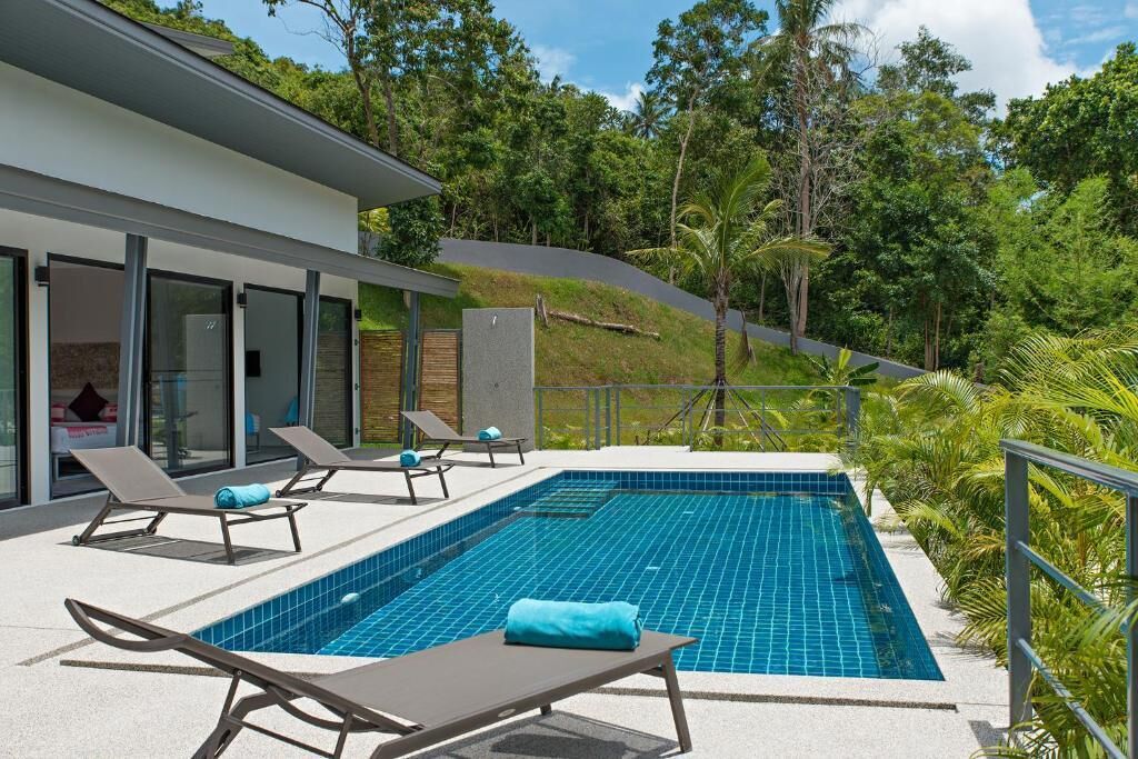 A modern pool area with lounge chairs and a view of a lush, green hillside.