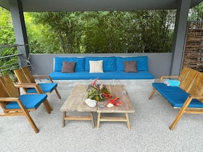 Een terras met een houten tafel, blauwe zittingen met kussens en een blauwe bank met kussens.