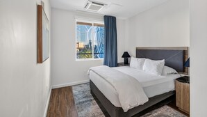 Una habitación de hotel moderna con una cama grande, una mesita de noche, una ventana con cortinas y vistas a la ciudad.