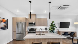 Una cocina moderna con una isla central, electrodomésticos de acero inoxidable y un televisor de pantalla plana montado en la pared.