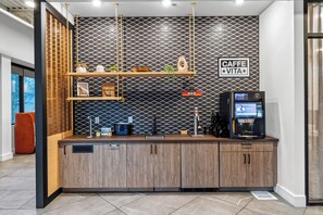 Un moderno bar de café con una pared negra con estampado, una máquina de café y un letrero que dice 'CAFFE VITA'.