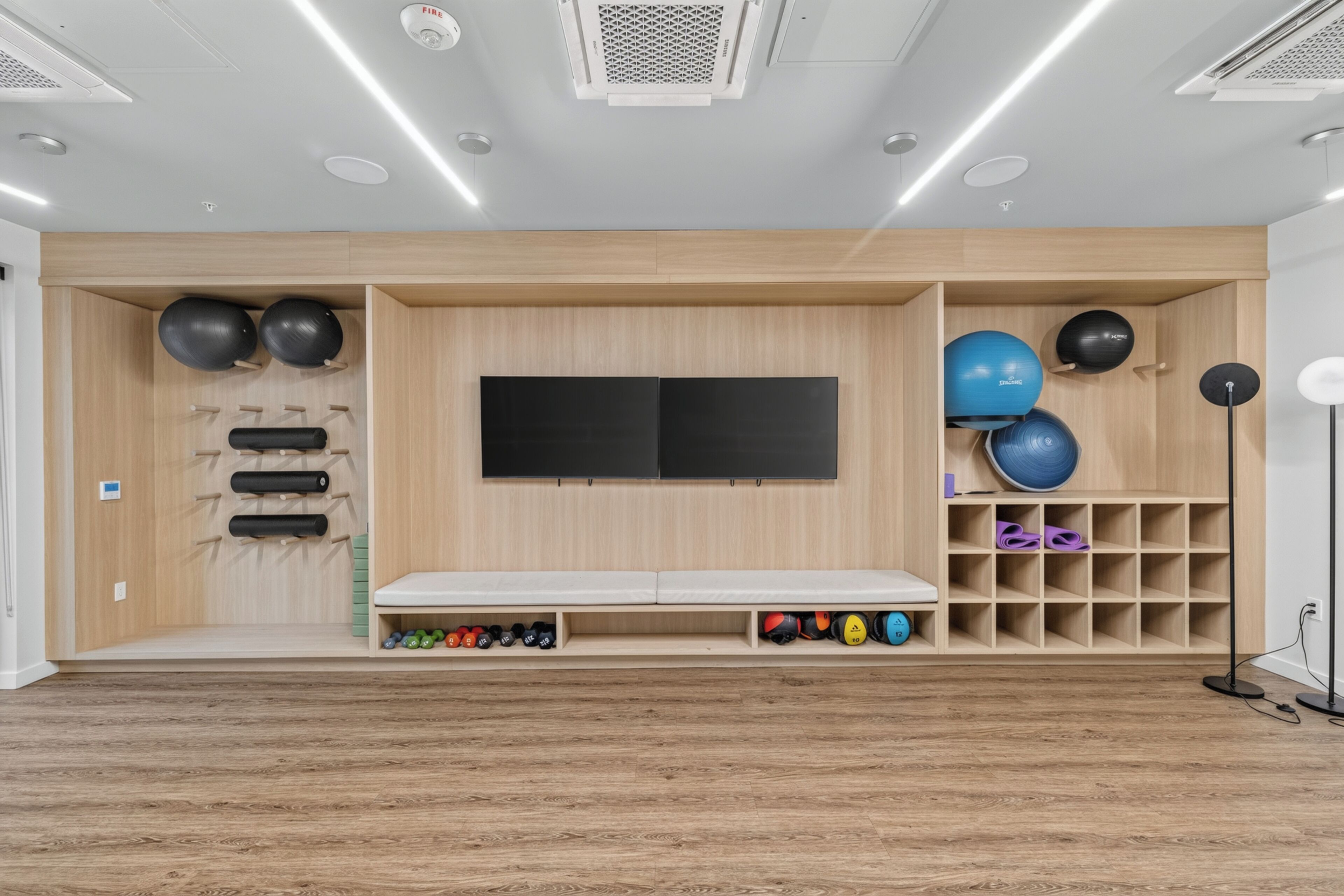 A room with a wooden wall unit, a flat-screen TV, a bench, and shelves with sports balls.