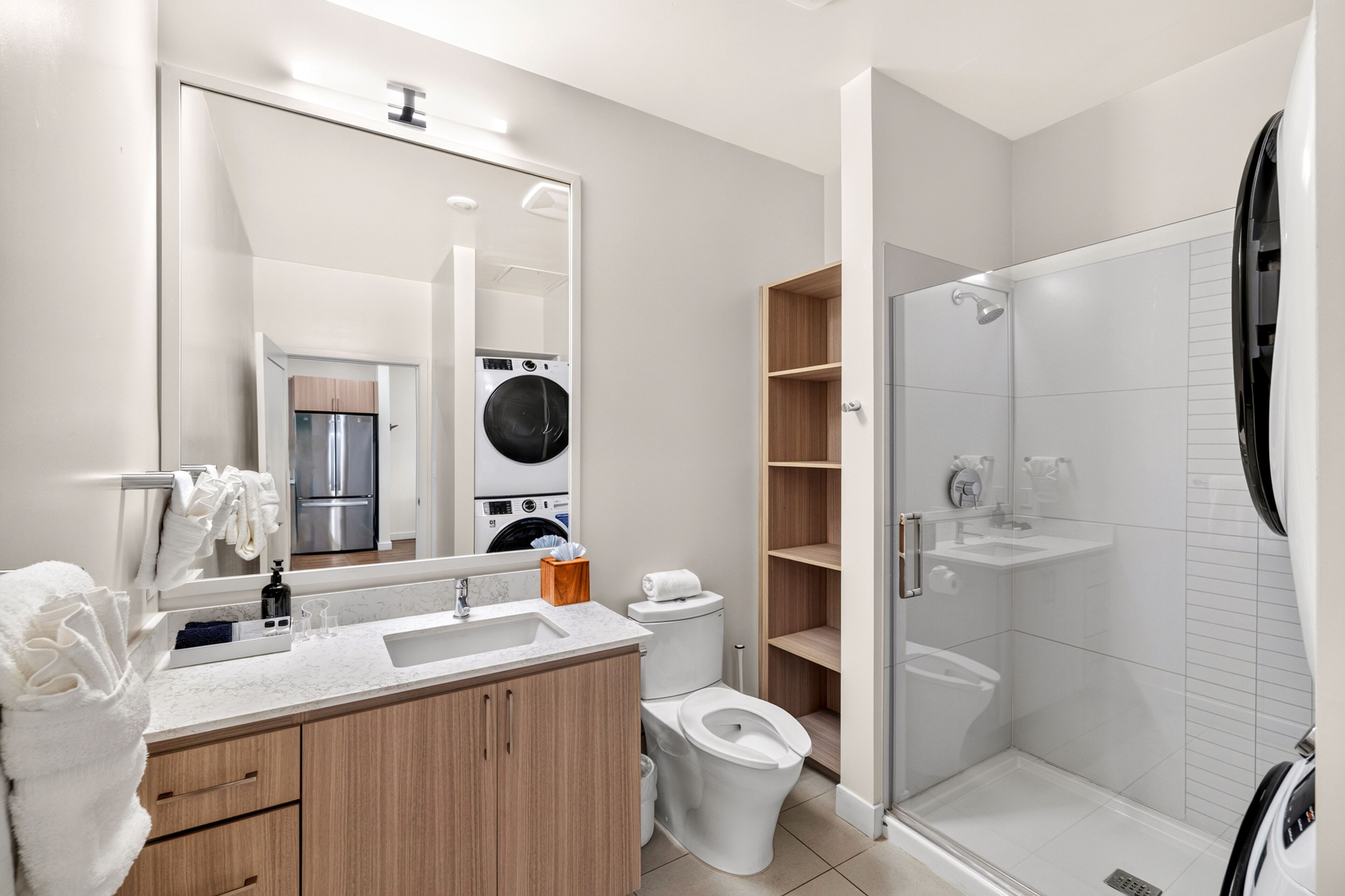 A modern bathroom with a large mirror, a sink, a toilet, a shower, and a built-in washing machine.