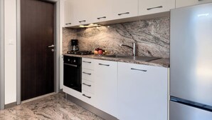 Une cuisine moderne avec des meubles blancs, un pare-feu en marbre, un réfrigérateur en acier inoxydable et un four encastré.