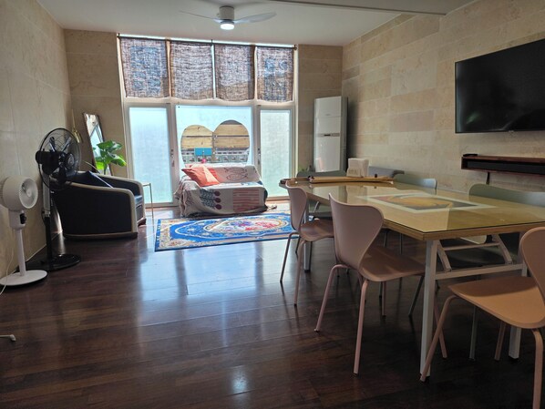 A modern living room with a glass table, comfortable seating, a large window, and a flat-screen TV.