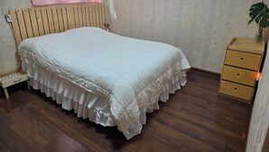 Un dormitorio con una cama de madera, una mesita de noche, un aparador, un radiador y una ventana con cortina.