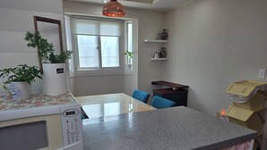Una cocina con encimera de granito, microondas, lavabo, ventana con persianas, planta en maceta y un taburete de madera.