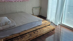 A bedroom with a bed on a wooden platform, a small metal table, a pink curtain, and a window with a white curtain. - MurMum 2 (Chilgok)