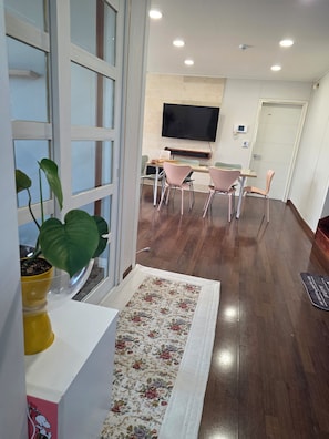 A modern interior with a dining area, a flat-screen TV mounted on the wall, and a potted plant by the window.