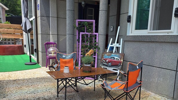 Un patio al aire libre con una mesa y sillas, un soporte para planta morado y un banco de madera.