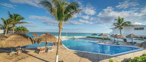 Zona de piscina con sillones de descanso, palmeras y vista al océano.