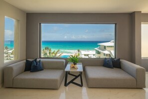 Een moderne woonkamer met twee banken gericht op een groot raam met uitzicht op een strand en oceaan.