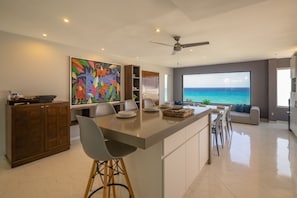 A modern kitchen with a large island, bar stools, a dining area, and a view of the ocean. - Walk to the Beach - Family Condo 2409 (Cancún)