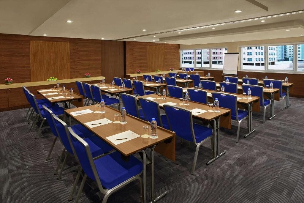 A conference room with multiple tables and chairs, equipped with water bottles and papers, and a view of buildings through large windows.