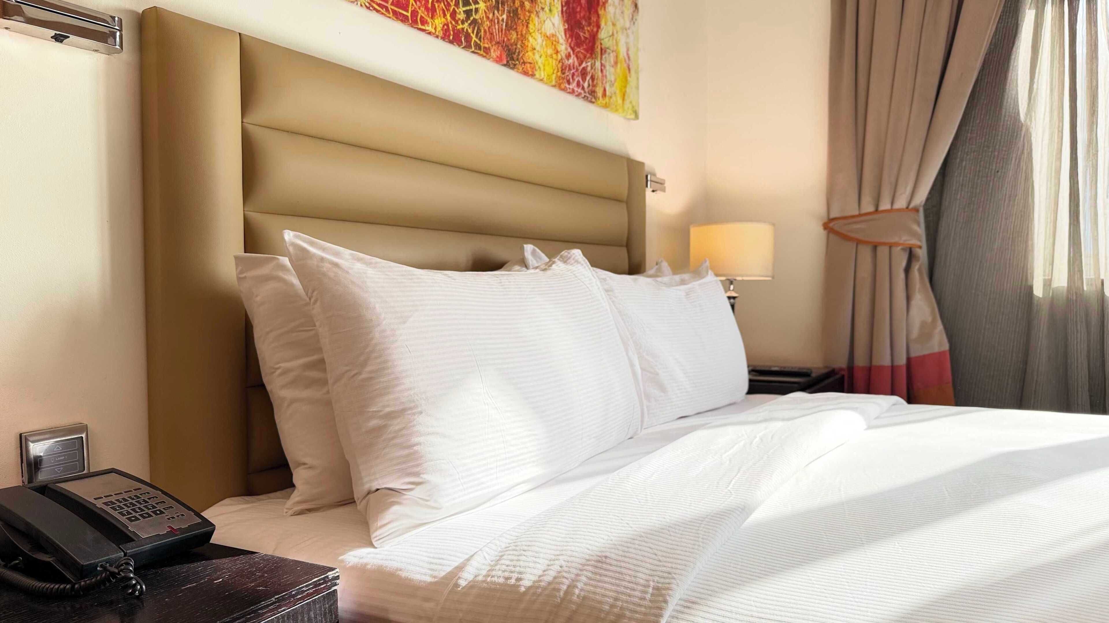Een hotelkamer met een bed, een bedtafeltelefoon, een lamp en een schilderij aan de muur.