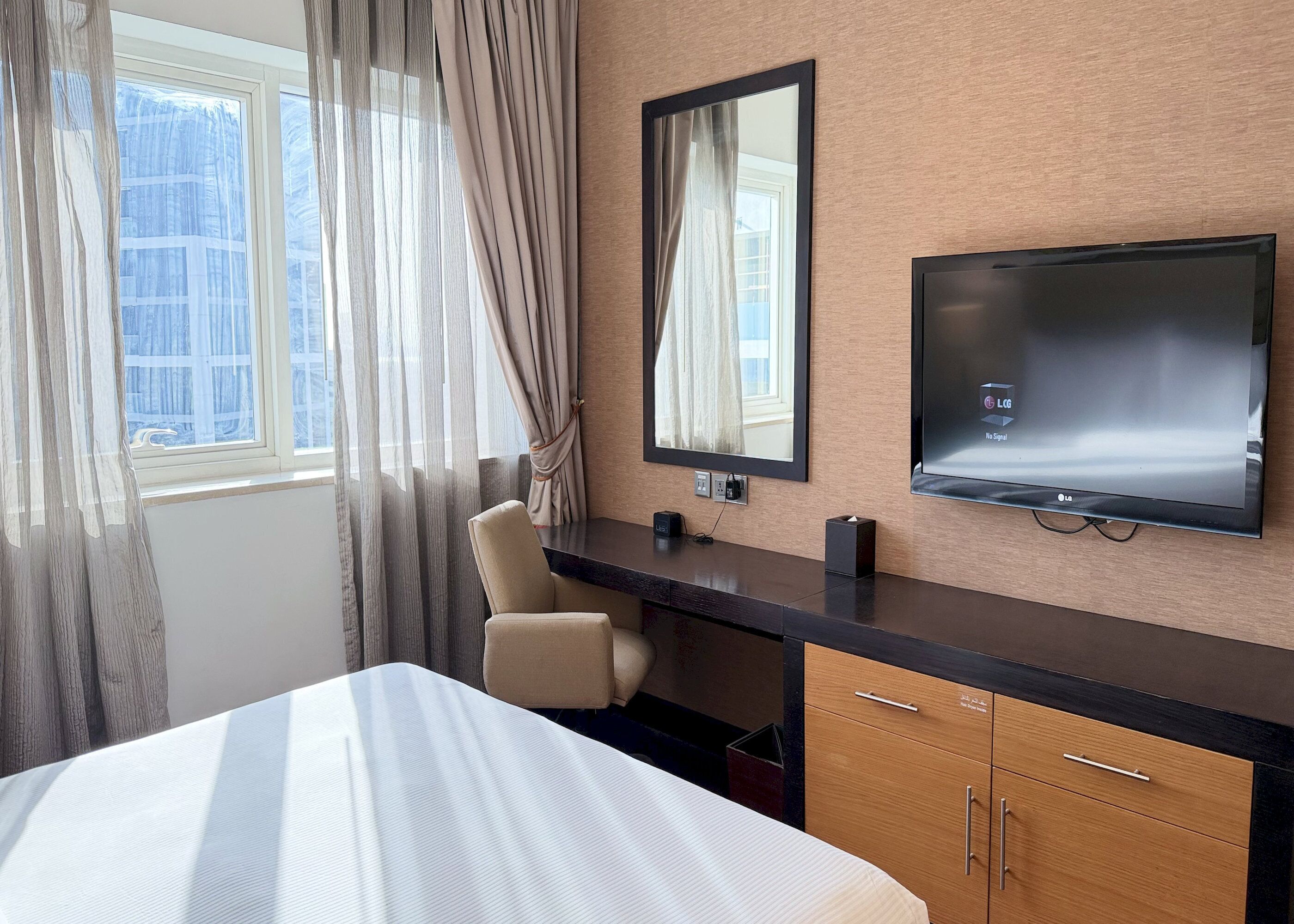 A hotel room with a bed, a desk, a chair, a TV, and a window with curtains.