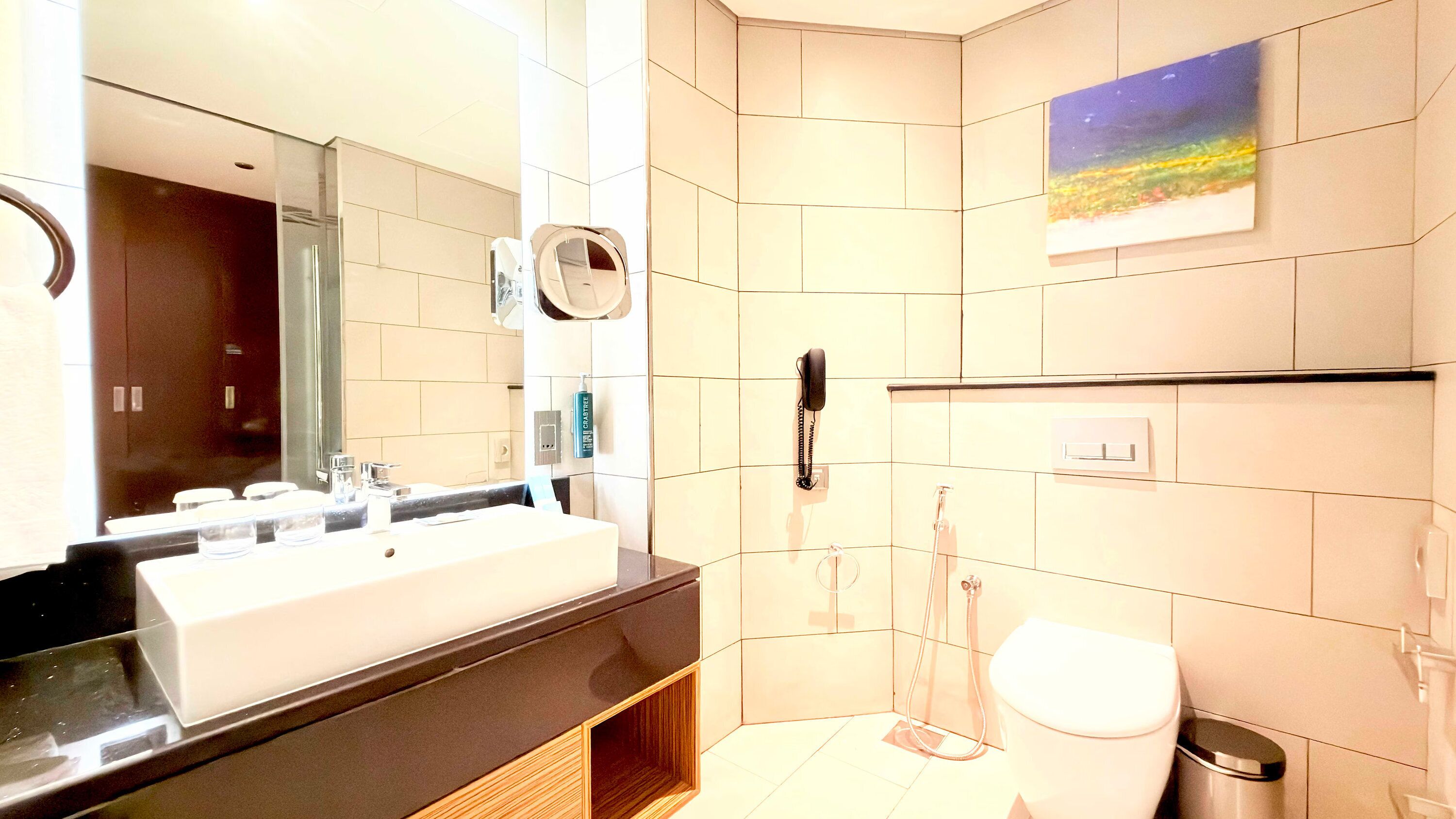 A modern bathroom with a large mirror, a sink, a toilet, and a shower.