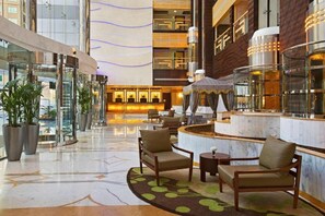 A hotel lobby with a reception desk, seating area, and a glass elevator.