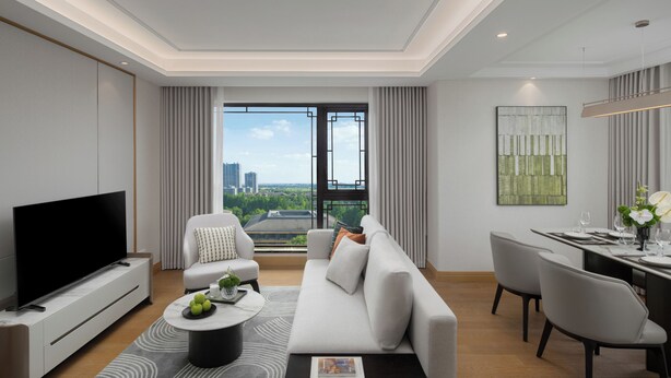 Una sala de estar moderna con un televisor de pantalla plana, un sofá, un comedor con una mesa dispuesta para dos personas y un ventanal con vistas a la ciudad.