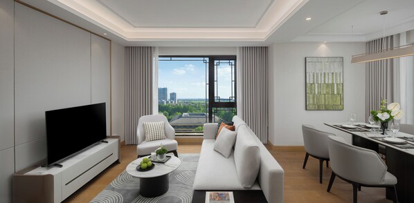 A modern living room with a flat-screen TV, a sofa, a dining area with a table set for two, and a large window with a city view.