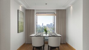 Un área de comedor con una mesa lista para dos personas, vista a la ciudad a través de un ventanal grande y una obra de arte enmarcada en la pared.