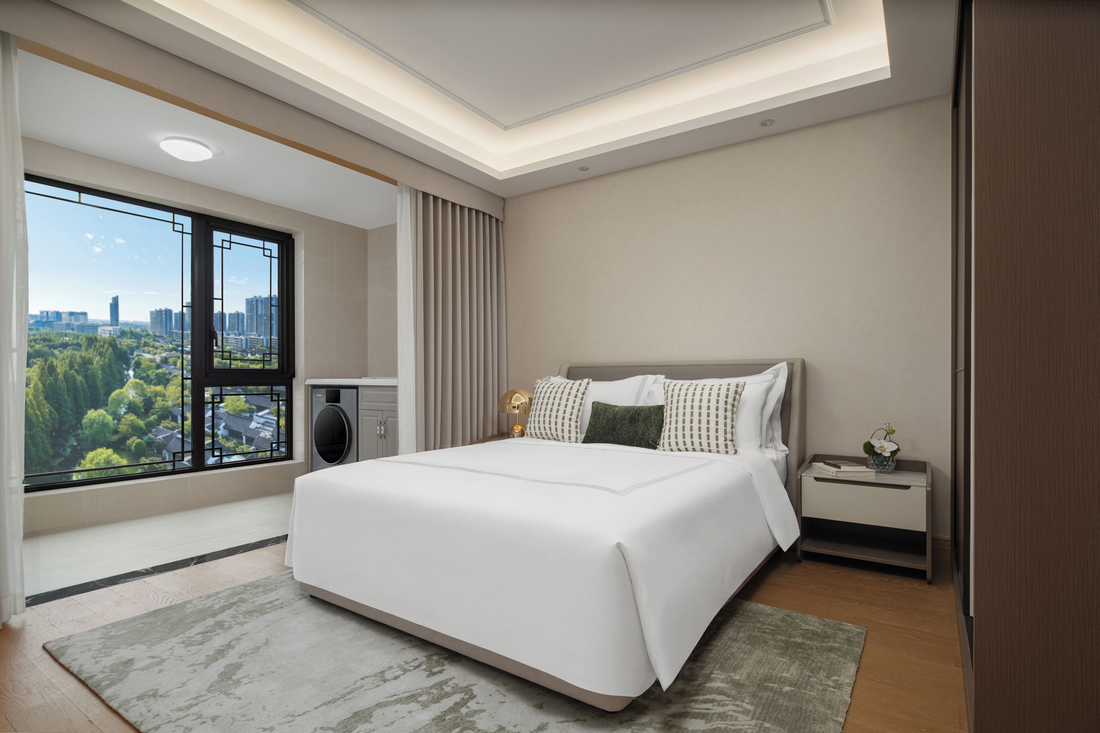 A modern hotel room with a large bed, a bedside table, a nightstand, a window with a city view, and a ceiling light.