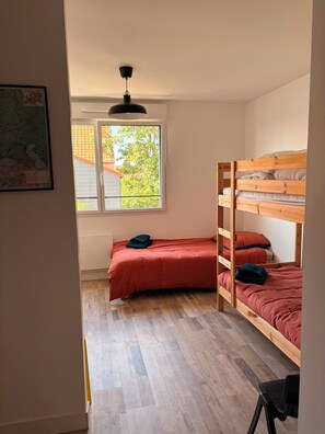 A room with a bunk bed, a single bed, a window with a view of trees, a map on the wall, and a ceiling light. - Beaulieu Le 15 Vacation Rental – Ambleteuse (sleeps 15) (Ambleteuse)