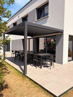 Une terrasse extérieure moderne, dotée d’une pergola, d’une table à manger et de chaises.