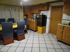 A kitchen with wooden cabinets, a refrigerator, a dining table with chairs, and a tiled floor. - Yellow House Near the Historic Center (Durango)