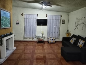 A living room with a fireplace, a black sofa, a glass coffee table, and a ceiling fan. - Yellow House Near the Historic Center (Durango)