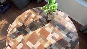 Una mesa redonda de madera con un diseño geométrico, una planta en maceta y una ventana al fondo.