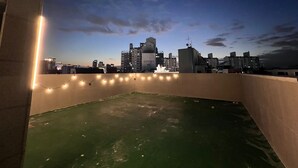 Terraza en la azotea con vistas al horizonte de la ciudad, luces colgantes y una fuente de agua.