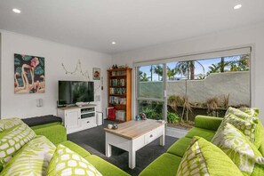Een moderne woonkamer met een flatscreen televisie, een boekenkast en groene gestoffeerde banken.