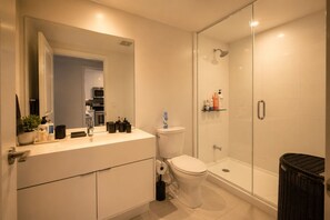 A modern bathroom with a glass shower enclosure, a white toilet, and a sink with toiletries.