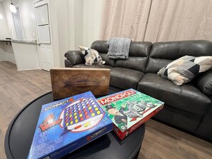 A living room with a leather couch, a coffee table, and three board games: Connect 4, Chess & Checkers, and Monopoly.