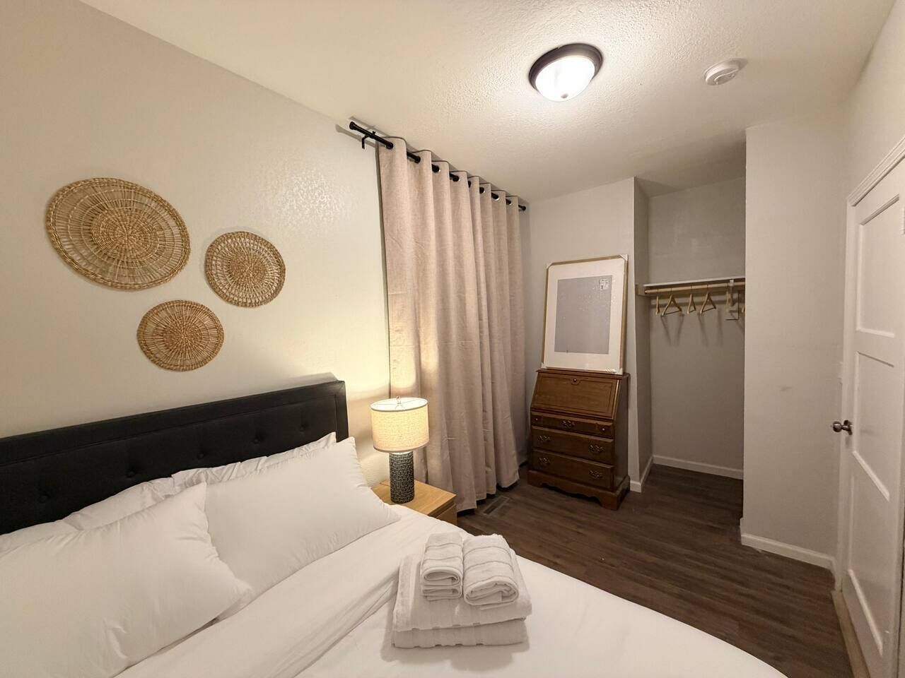 A hotel room with a bed, a nightstand with a lamp, a dresser, a mirror, and a door.