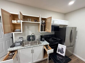 A modern kitchen with white cabinets, a stainless steel sink, a black stove, and a built-in refrigerator.