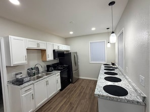 A compact kitchen with white cabinets, a stainless steel refrigerator, a built-in oven, and a granite countertop. - EKO Stays | Downtown MKE Group Retreat Near Fiserv (Milwaukee)