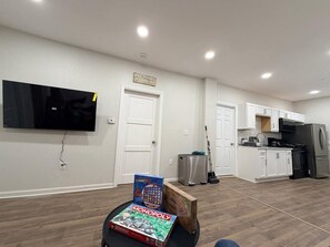 A modern kitchen with white cabinets, a stainless steel refrigerator, and a flat-screen TV mounted on the wall. - EKO Stays | Downtown MKE Group Retreat Near Fiserv (Milwaukee)
