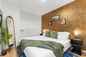 Et hotelværelse med en seng, et natbord, en lampe, en plante og et spejl.