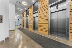 Un espace d’ascenseur moderne avec des panneaux métalliques et en bois, un sol poli et un bouton d’urgence bien visible.