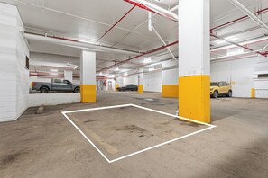 En parkeringskælder med flere etager, beton gulve, gule og hvide søjler og parkerede køretøjer.