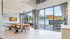 Um quarto amplo com uma mesa de jantar grande, um sofá e vista para o exterior por grandes janelas.