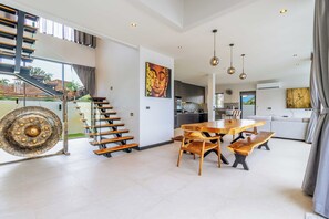 Un vaste espace de vie comprenant une table à manger, des bancs, un escalier et une grande fenêtre.