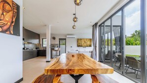Interior moderno com mesa de jantar de madeira, cozinha e grandes janelas.