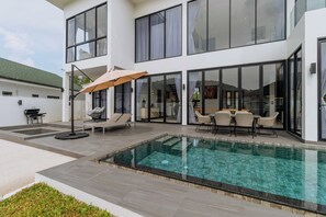 Une maison moderne dotée d’une piscine, d’un espace salon extérieur et de grandes fenêtres.
