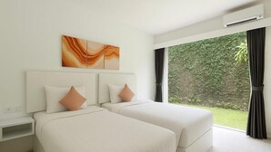 Quarto de hotel com duas camas, mesa de cabeceira, ar condicionado fixado na parede e uma janela grande com vista para área verde.