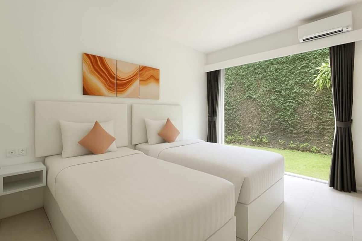 A hotel room with two beds, a nightstand, a wall-mounted air conditioner, and a large window with a view of greenery.