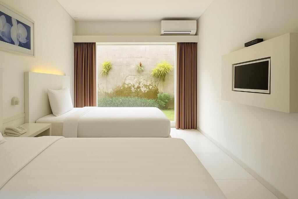 Habitación de hotel con cama, mesita de noche con lámpara, televisor montado en la pared y ventana con cortinas.