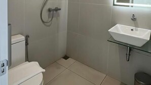 Casa de banho com sanita, chuveiro, lavatório e espelho.
